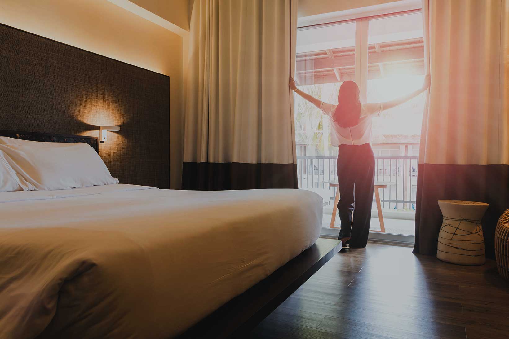 Guest enjoying the view as she opens the curtains in her hotel room, highlighting the comfortable and inviting ambiance provided by Broadband Hospitality